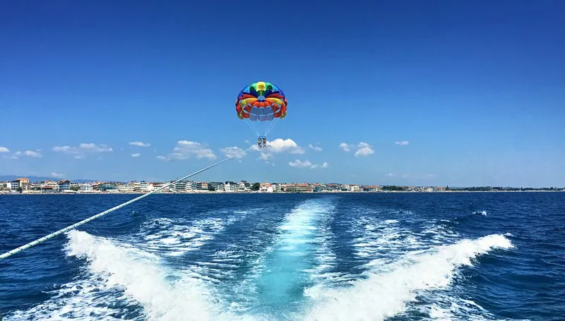 Two people parasailing over the sea on a sunny summer day, being pulled by a speedboat creating waves on the water’s surface. A perfect calm thrill seeking adventure.