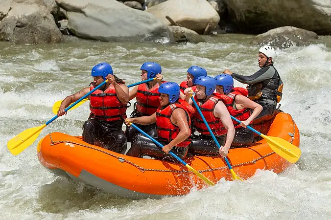 Group of adventurers White-Water Rafting down river rapids, paddling together through splashing waves on a fast-flowing river. A perfect action packed group thrill!